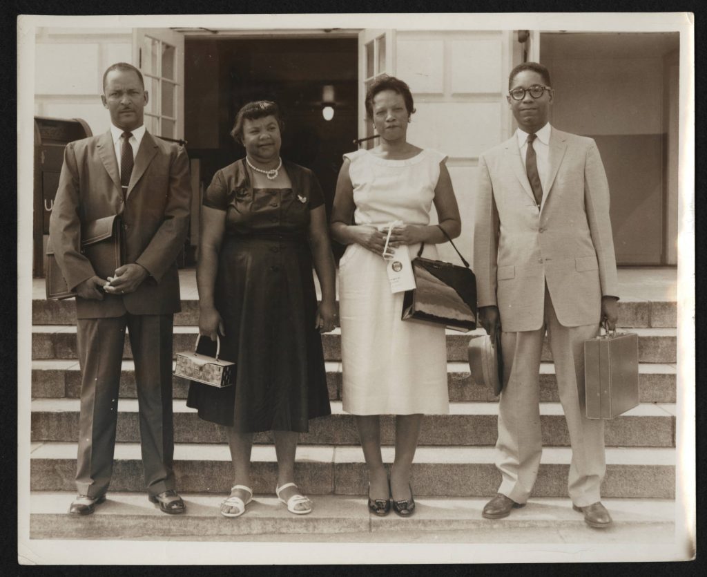 Two men in suits and two women in dresses stand on courthouse steps.